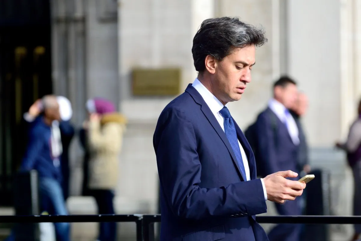 A man in a dark suit and blue tie looks down at his phone on a street in Westminster.
