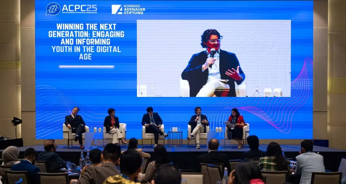 Ben Guerin, shown on a large screen, speaking on a panel titled “Winning the next generation: engaging and informing youth in the digital age” at the Asian Conference on Political Communications (ACPC25) in Singapore, with four other panellists seated below.