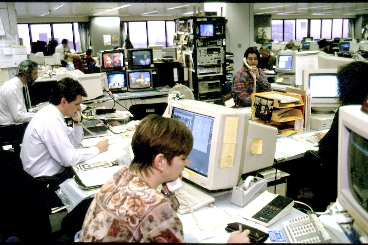 An office in 1994: staff on landline phones at desks crowded with beige CRT monitors and televisions.
